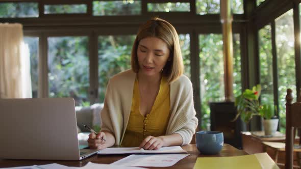 Asian woman sitting at table and working from home using laptop smiling