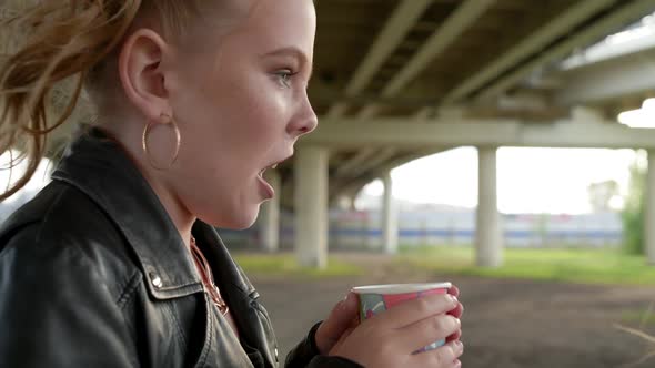 Frozen Punk Girl Holding in Hands Hot Drink for Warming on Urban Street