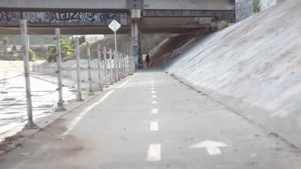 A young man riding his bicycle on a bike path by a creek.