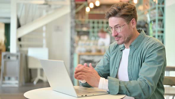 Middle Aged Man with Laptop Smiling at Camera in Cafe