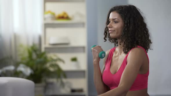 Young woman lifting dumbbells alternately, exercising, body care, weight control