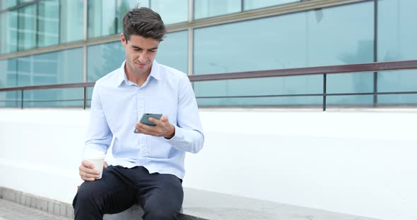 Businessman using mobile phone and holding cup of coffee