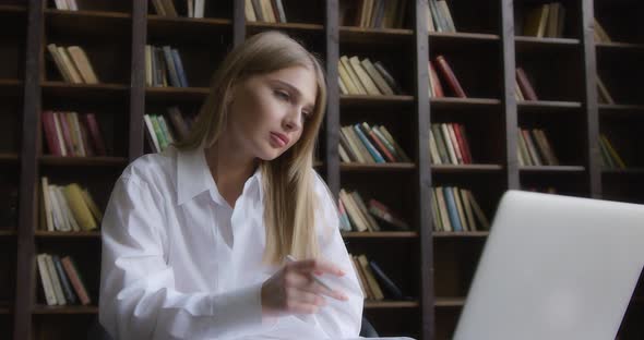 Business Woman in a White Shirt Works at a Laptop and Takes Notes