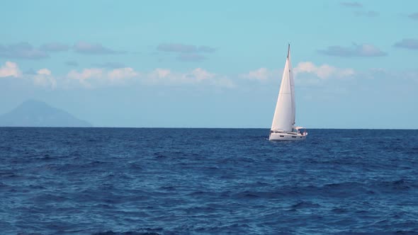 White Sailboat Sailing in Sea Against Blue Sky and Mountains