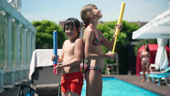 Side View of Confident Caucasian Children Standing at Swimming Pool with Water Gun Back to Back and