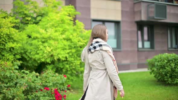 A young woman in a coat walks down the street, view from the back