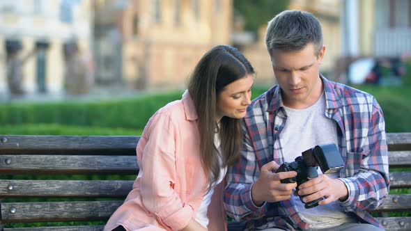 Young Couple Sitting on Bench, Watching Photos From Tourist Trip on Camera