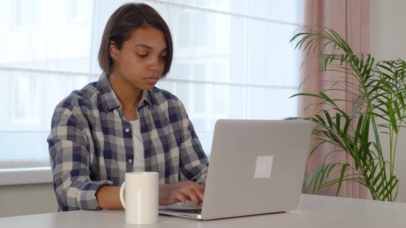 Young Woman Sitting at a Computer Desk Using a Laptop Working Online at Home