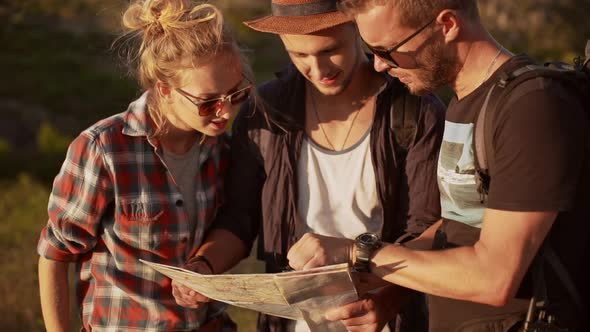 Three Friends Looking for Right Way Staring at Map and Compass Outdoors in Slowmotion