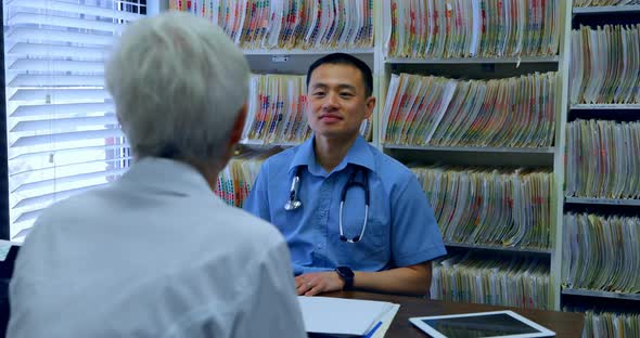 Young Asian male doctor and senior patient interacting with each other at clinic 4k