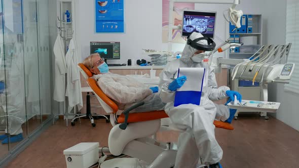 Dentist Assistant in Potective Suit Measuring Patient Temperature
