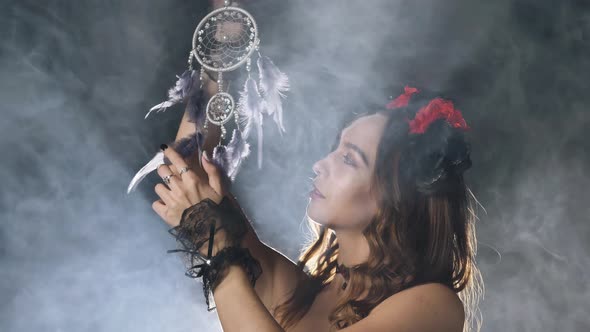 A Mystical Mysterious Woman in a Dark Suit and Halloween Makeup Turns a Dream Catcher in Smoke in