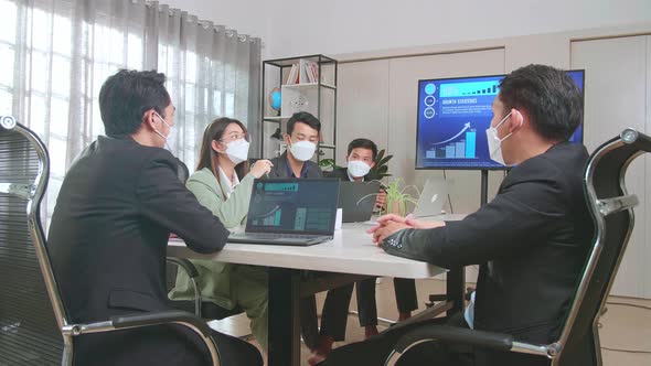 Asian Team Wear Face Mask Have Meeting In A Conference Room. They Share Opinions, Statistics On TV