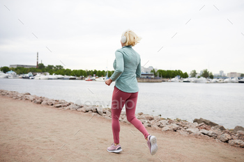 ening to music in headphones while jogging along waterside in the morning