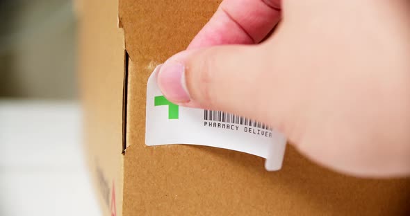 Hands applying +PHARMACY Sticker label on a shipping cardboard box.