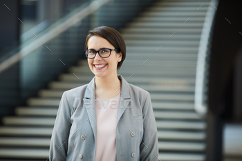 smile wearing gray jacket and eyeglasses standing in lobby and looking at camera