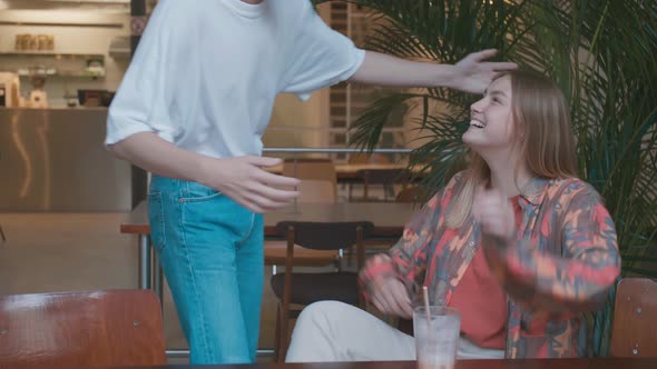 Happy Young Woman Greeting Male Buddy Coming at Meeting in Cafe, Laughing Give Fist Bump Say Hello