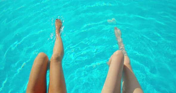 Young Women Sitting on Edge of Pool and Dangling Their Feet in Water. Two Girls with Slim Tanned