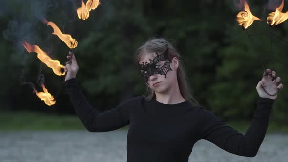 Portrait of Young Beautiful Woman in Mask Performing a Show with Flame in Front of Trees. Skillful