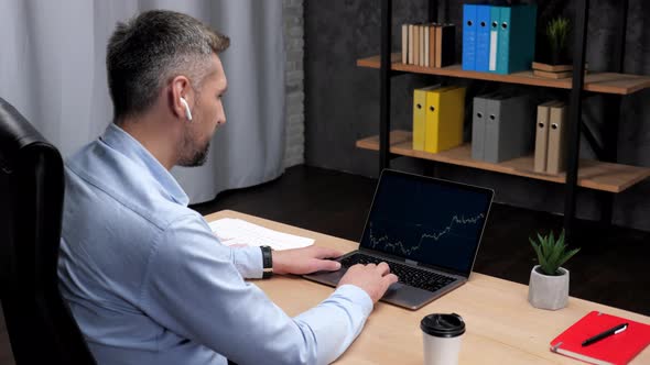 Smiling Man Professional Trader Broker Uses Laptop with Stock Exchange Chart