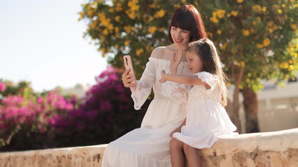 Mother and Daughter Taking Selfie on Smartphone While Sitting on Background on Tropical View