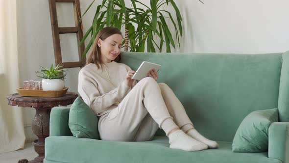 Beautiful Young Brunette Woman Using Tablet Sitting on Sofa at Home at Living Room