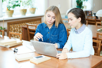 source while preparing for exam together in college library, confident girl with blond hair pointing at laptop screen