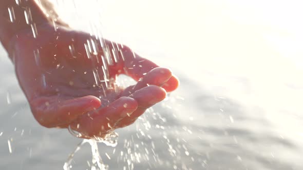 Female Cupped Hand Catches Falling Water Drops on Seascape Background