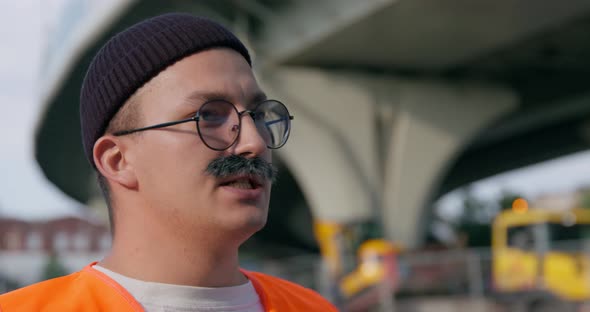 Builder with Thick Graying Mustache in Orange Visibility and Reflective Safety Vest Looks at