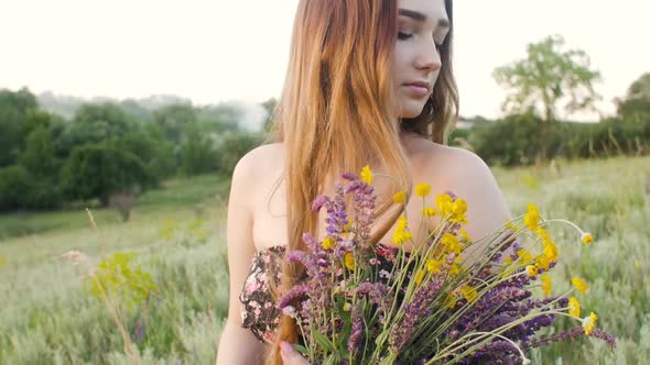 beautiful girl with bouquet of wildflowers on meadow, young woman with long hair in dress