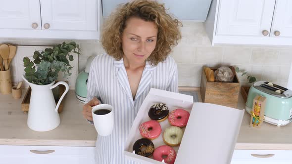 Young Woman Wearing Pajamas Having Breakfast With Coffee And Doughnut On Kitchen