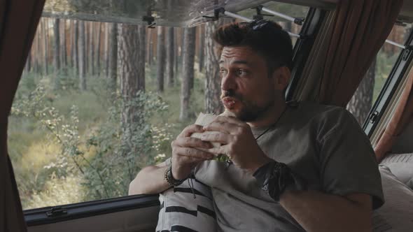 Hipster Man Enjoying Sandwich in Camper in Forest