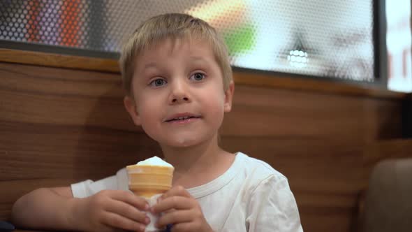 Adorable Little Caucasian Boy Eating Icecream Cone at the Table in Cafe