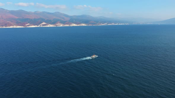 Aerial View of Small Ship Sailing Along Sea Bay, Mountains on Background