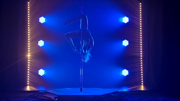 Acrobatic Exercises on a Pole. Silhouette of a Young Woman Practicing Sports Pole Dance. Blue Smoky