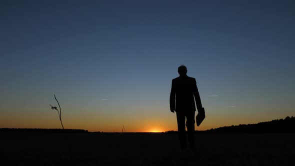 Silhouette of Businessman with Briefcase Walking Across Field at Sunset