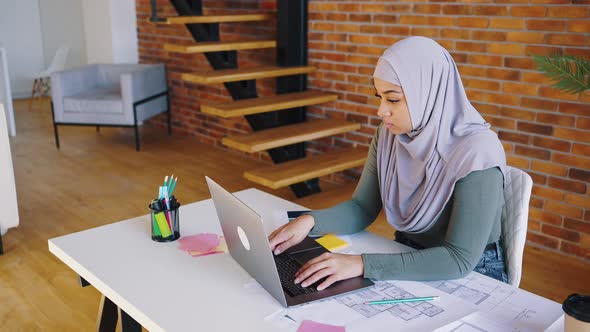 Islamic Woman in Hijab Works with Laptop While Sitting at Her Desk at Home