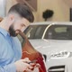 Happy Man Texting on a Smart Phone While Shopping for New Car at the Dealership - VideoHive Item for Sale