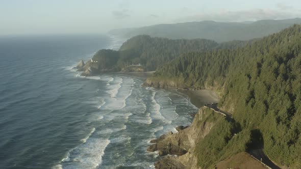Aerial along rugged Oregon coast with highway and Haceta Head lighthouse in the distance
