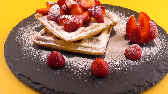 Belgian waffles with strawberry and powdered sugar on a stone board on an orange background