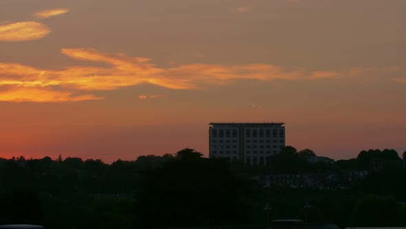 Wide 30 second dawn timelapse of a tall office building and trees silhouetted into the foreground.