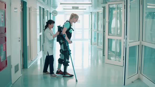 Nurse is Helping a Female Patient to Move in the Exoskeleton