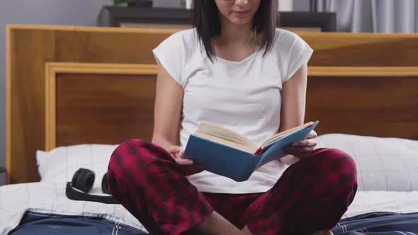  woman in glasses which sitting on bed in contemporary bedroom and reading book