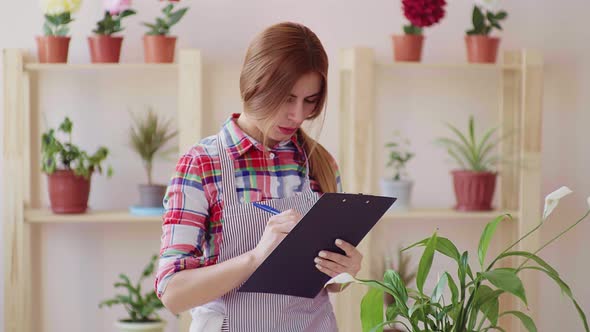 Small Business. A Girl in a Plaid Shirt and a Striped Apron Holds a Folder for Papers and Writes