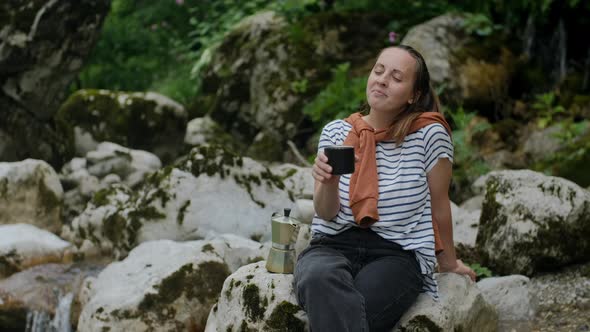 Peaceful Woman with close eyes enjoys nature and drinks coffee  from Mocha Pot against mountain rive