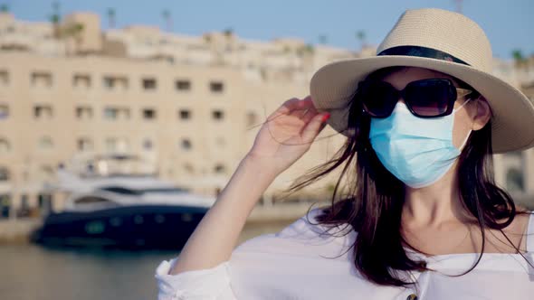 Young Woman in Protective Mask, Summer Clothes, Sunglasses and Sun Hat, on the Background of a Yacht