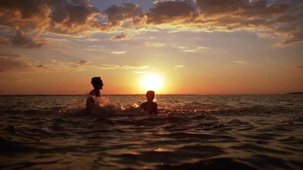 Silhouettes of Two Cheerful Boys 1012 Having Fun and Splashing Water Together While Swimming in Sea