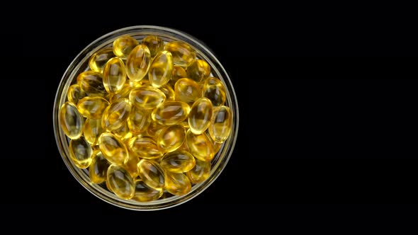 Gold oil capsules Omega 3 on black background, rotation