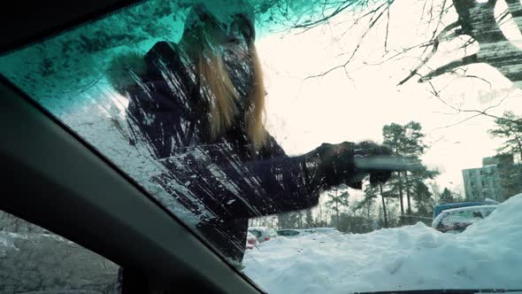 Young Woman with Snow Brush Scraping Ice From Windshield of Car