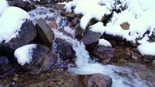 Small Stream Among Wet Stones and White Snow in the Picturesque Carpathian Mountains in Ukraine